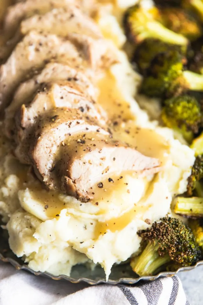A close up of Dijon Pork Tenderloin piled on mashed potatoes and roasted broccoli on the side.