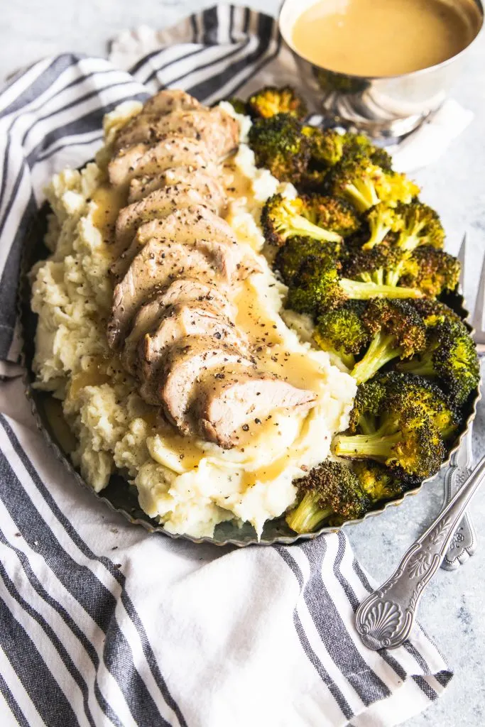 A platter of Dijon Pork Tenderloin piled on mashed potatoes and roasted broccoli on the side.