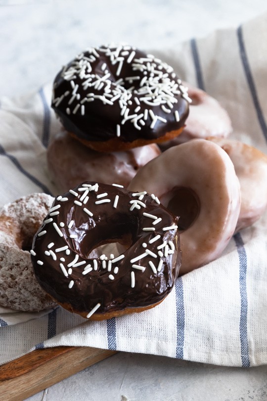 Sourdough donuts  piled together that are glazed, dipped in powdered sugar, and covered with chocolate icing.