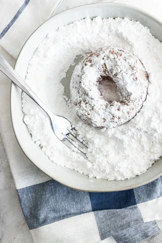 Dipping the hot donut into powdered sugar helps create a more even, thick coating.
