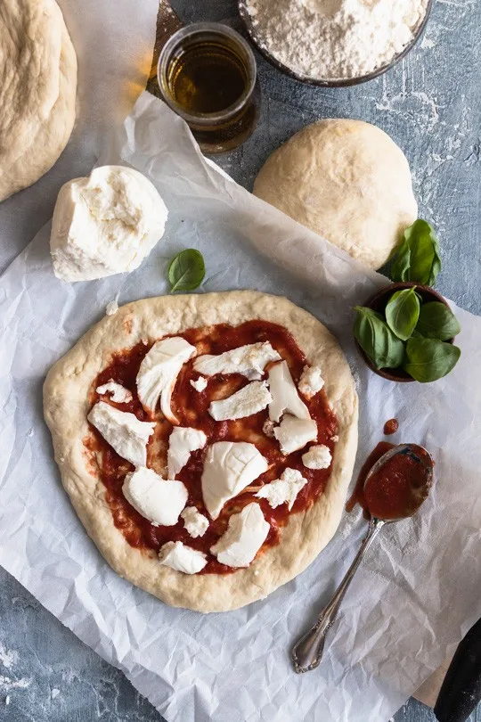 An uncooked pizza with fresh mozzarella chunks on top and basil leaves scattered around.