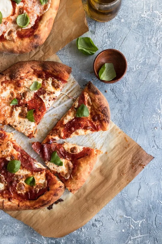 A sourdough crust pizza topped with mozzarella, slices of salami and pepperoni, and fresh basil leaves.