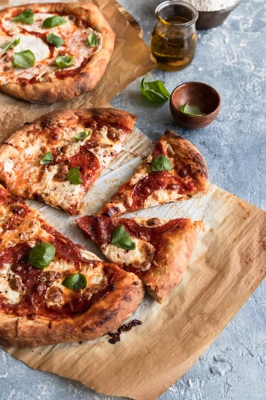 A sourdough crust pizza topped with mozzarella, slices of salami and pepperoni, and fresh basil leaves.