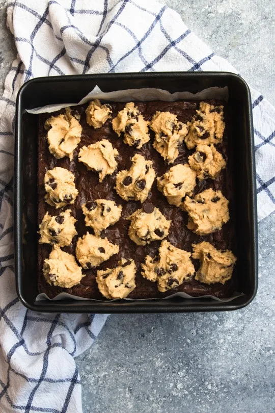 Small scoops of edible cookie dough on a pan of brownies, waiting to be spread over the top.