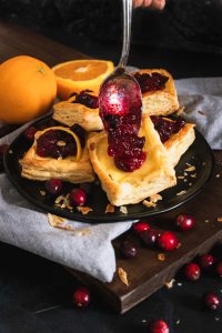 Cranberries being spooned onto cream cheese filled puff pastry square
