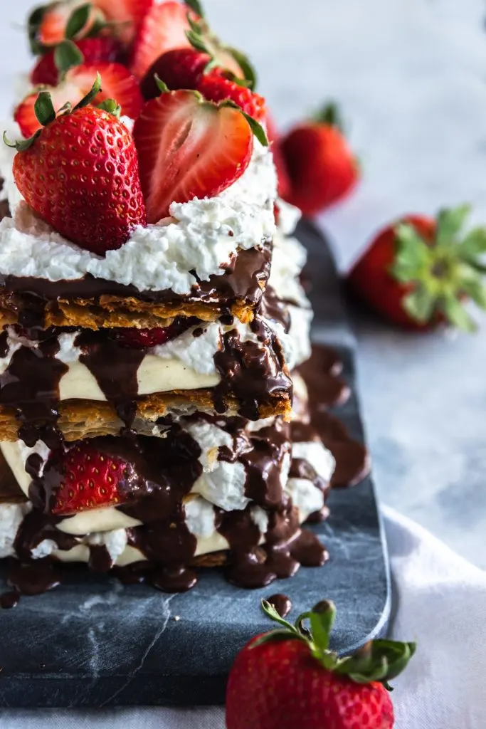 A strawberry napoleon dessert with layers of puff pastry, pastry cream, whipping cream, fresh strawberries, and chocolate ganache.