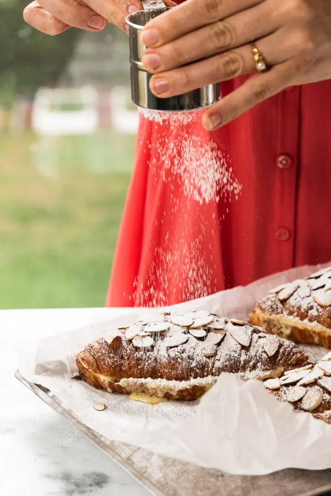 Sprinkling powdered sugar over freshly baked almond croissants.