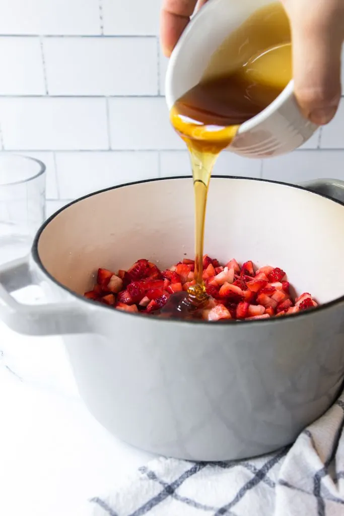 Pouring honey into the pot the strawberries, water, and lemon juice.