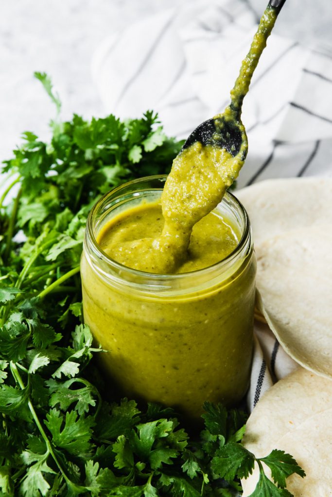 A jar of green enchilada sauce with some running off a spoon.