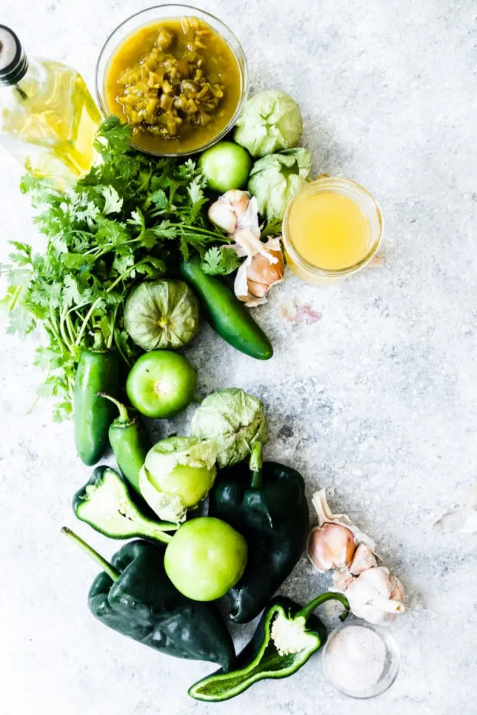 The ingredients needed for green enchilada sauce--poblano peppers, jalapenos, tomatillos, garlic, cilantro, canned green chilis, salt, broth, sea salt, and olive oil.