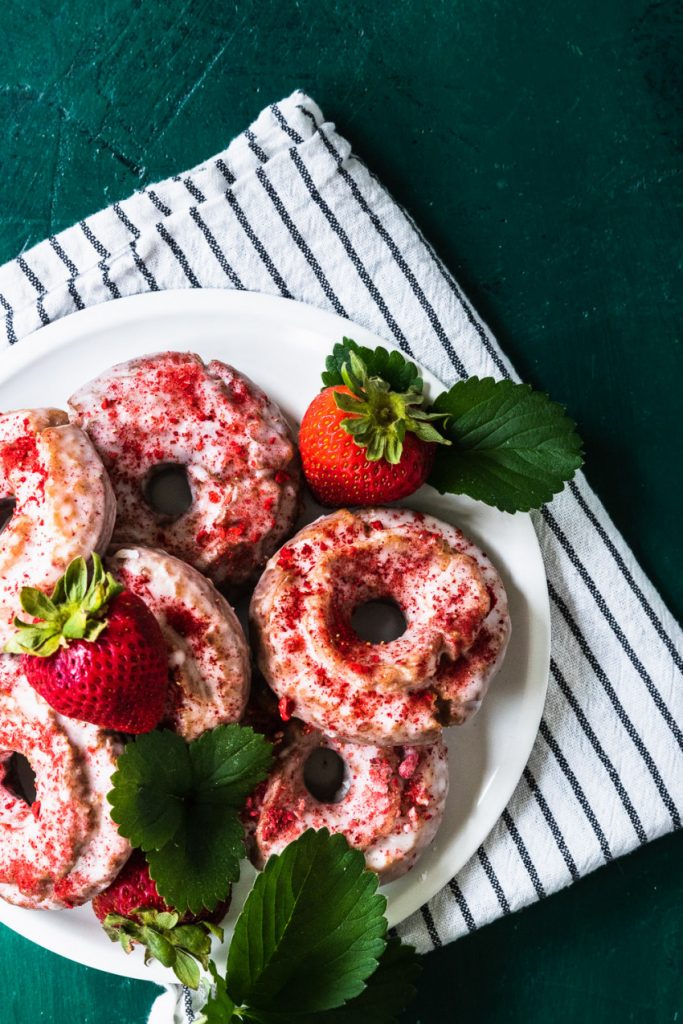 A stack of glazed old-fashioned strawberry donuts, sprinkled with powdered strawberries.