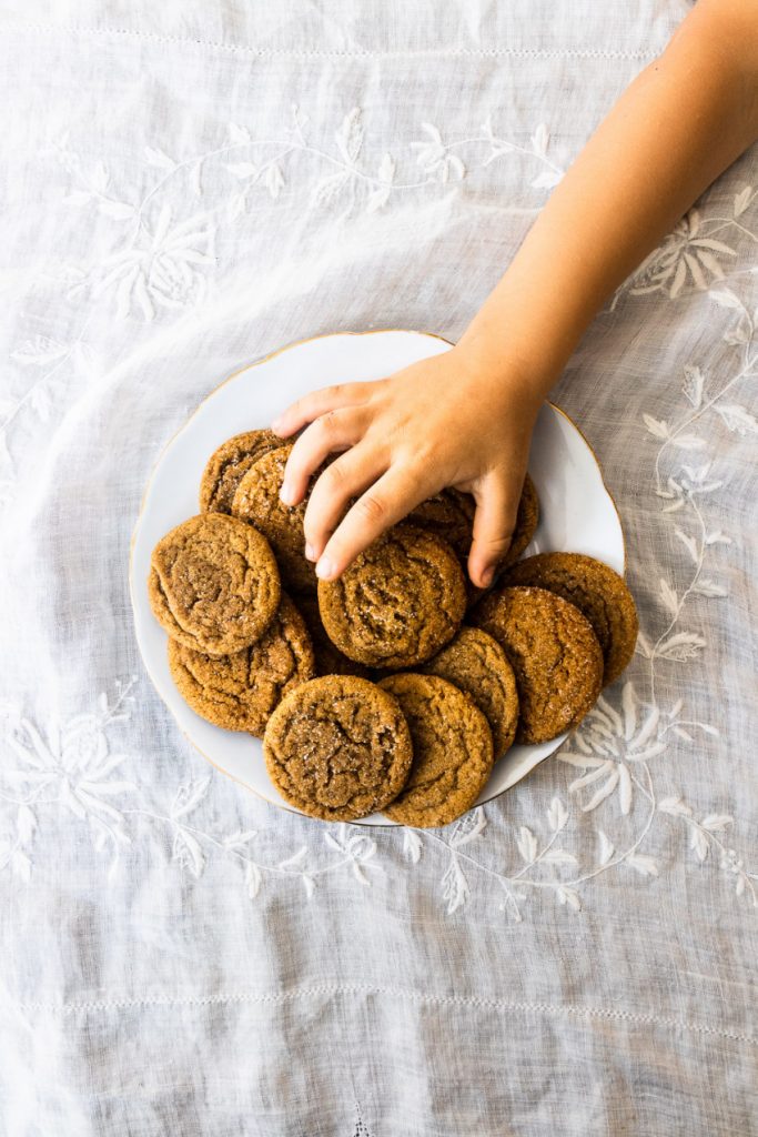 A plate of chewy, soft gingersnaps with a child's hand reaching in to take one.