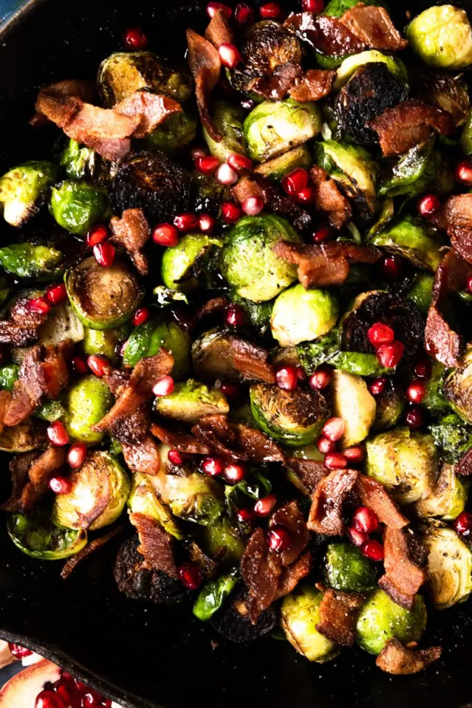 A close up of pan seared brussels sprouts and bacon with pomegranate molasses and pomegranate arils.