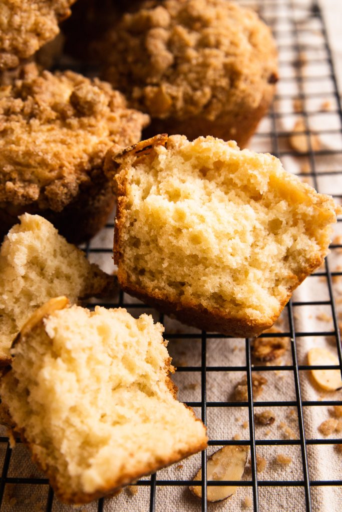 A coffee cake muffin topped with crumb topping and broken open to show a tender, moist crumb.