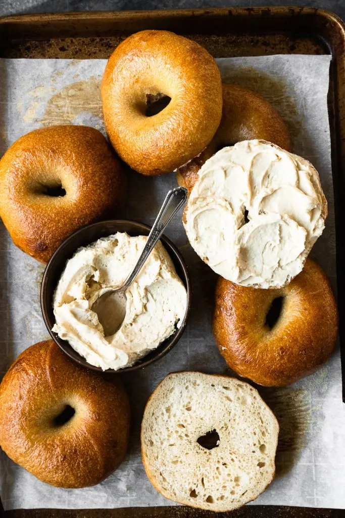 A tray of freshly baked, easy sourdough bagels with a bowl of cream cheese spread.