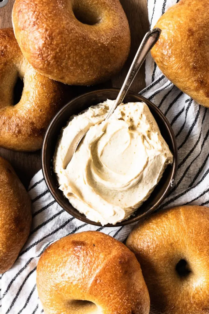 A swirly bowl of cream cheese spread, surrounded by bagels.