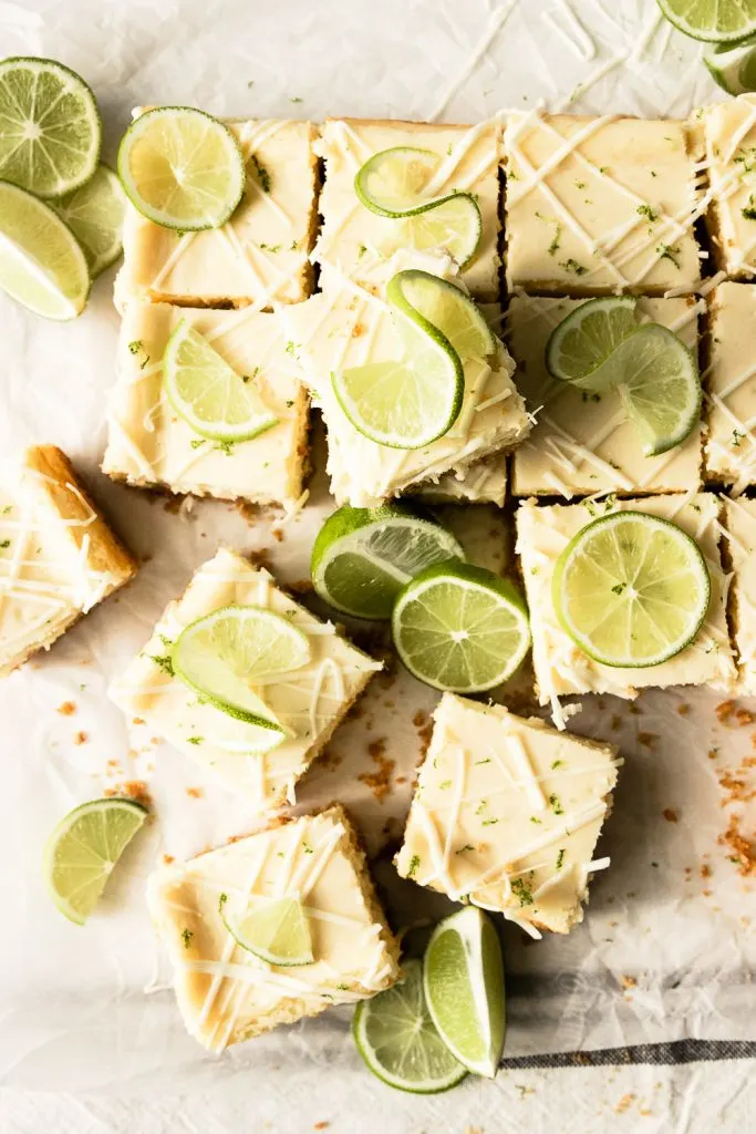 A pan of White Chocolate Lime Cheesecake Bars, cut into squares and decorate with drizzled white chocolate and limes.