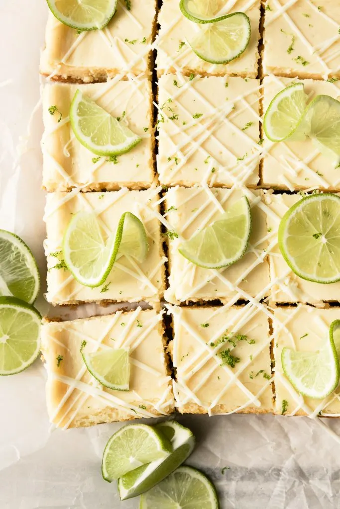The white chocolate lime cheesecake bars cut into squares and decorated with drizzled white chocolate and garnished with thinly sliced limes.