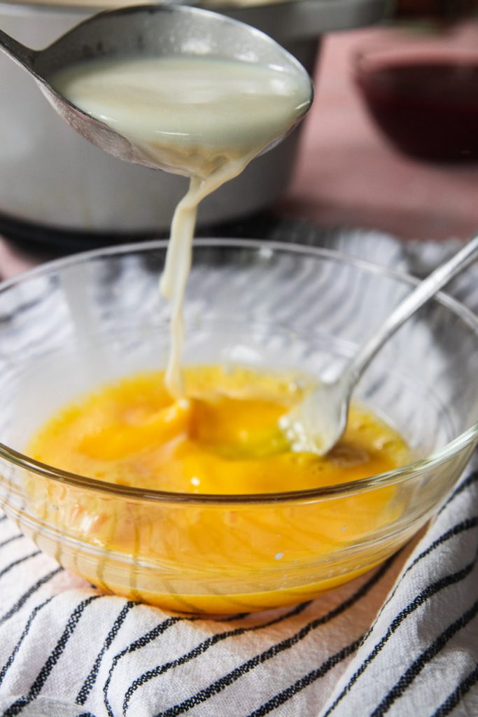 Tempering the egg yolks by slowly pouring in hot cream while whisking.