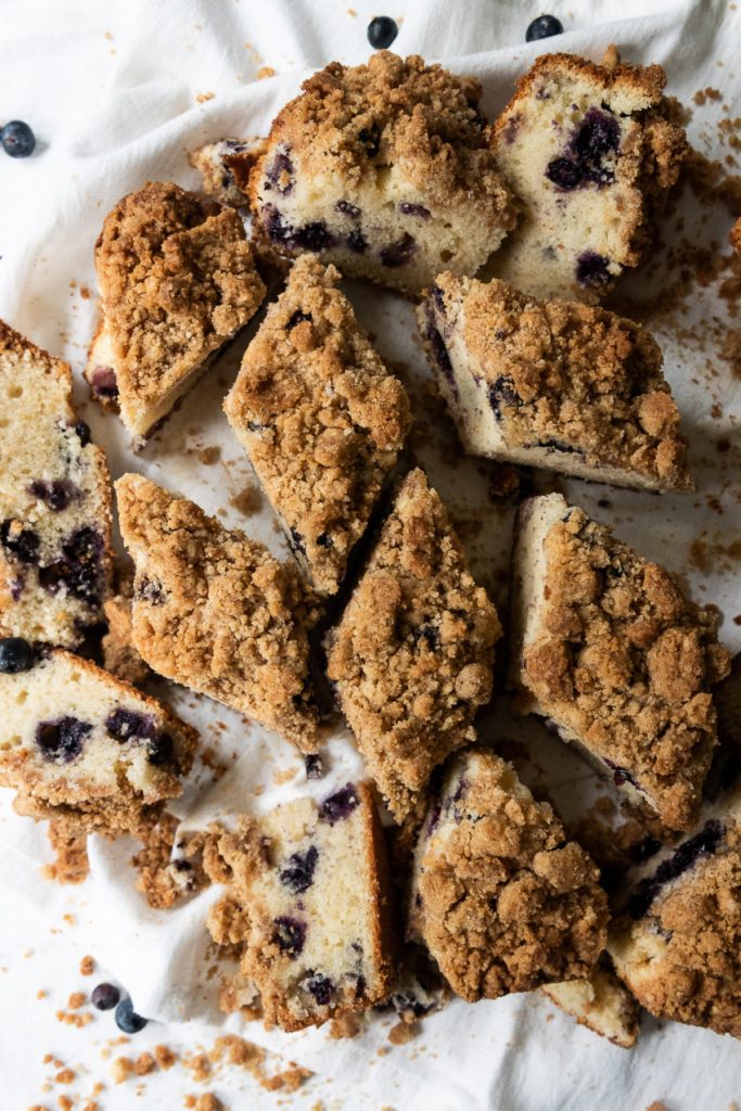 A sour cream blueberry coffee cake with a crumb topping, cut into pieces.