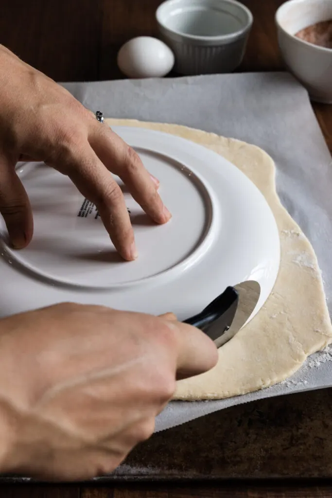 With a large plate as a template and wheel cutter, cut a sheet of puff pastry into a circle. 