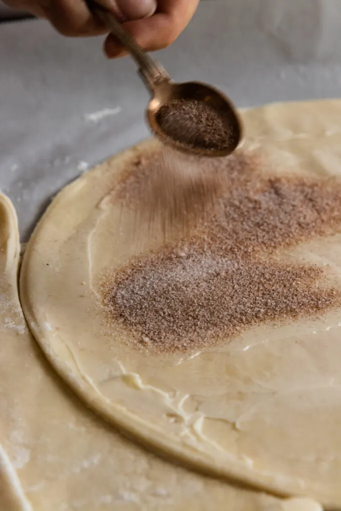 Sprinkling a generous amount of cinnamon sugar over the buttered puff pastry.