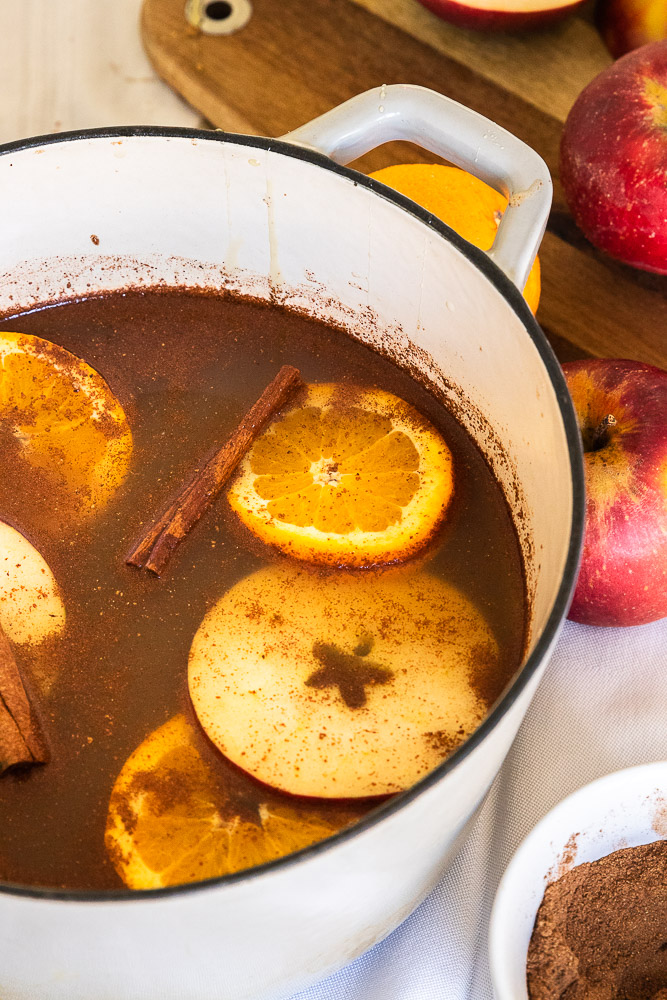 A pot of chai apple cider, topped with apple and orange slices and cinnamon sticks.