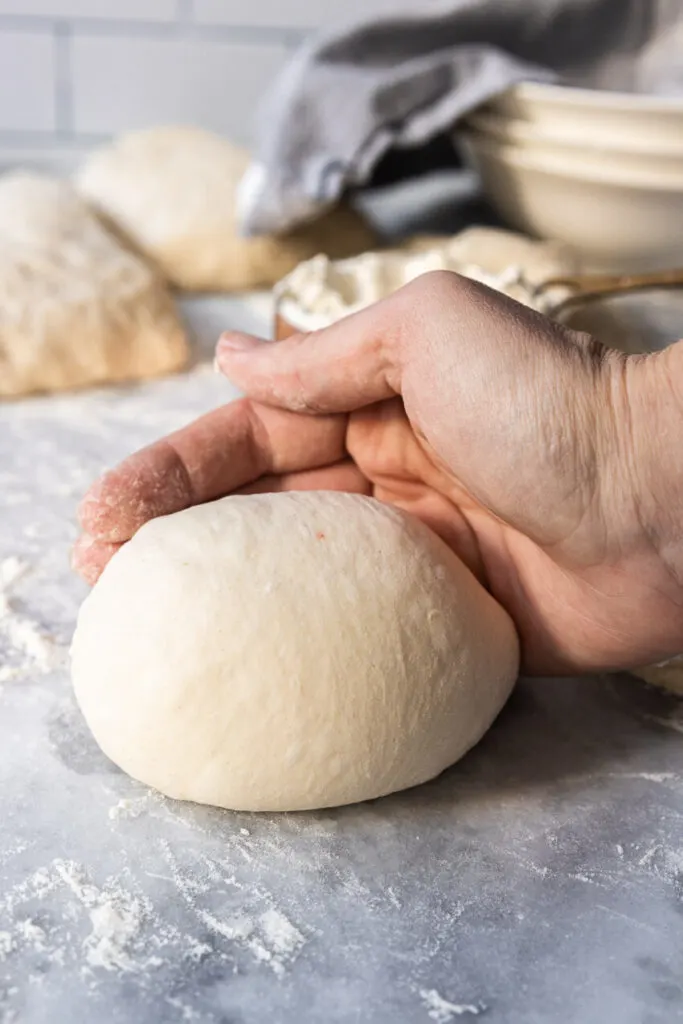 Using the edge of your hand to push the dough across the counter, creating gluten tension around the dough.