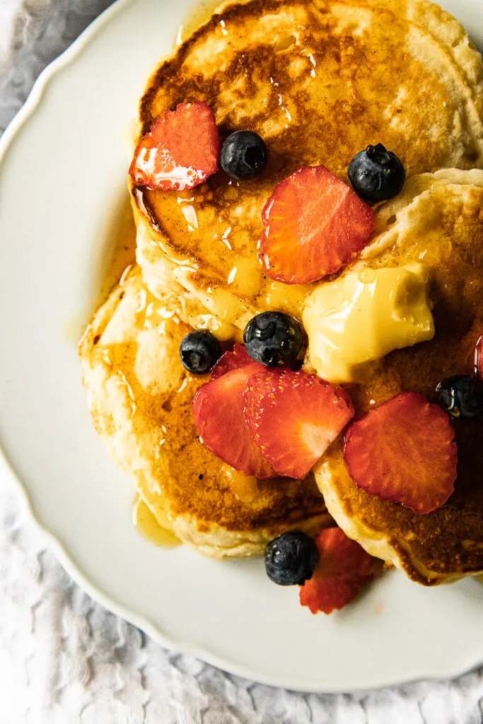 A plate of pancakes, topped with pancakes, berries, and vanilla bean maple syrup.
