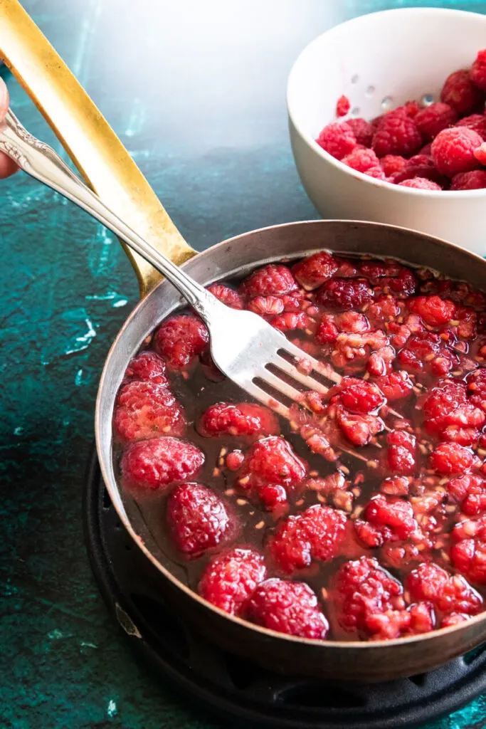 Mashing the raspberries with a fork after adding them to the pan.