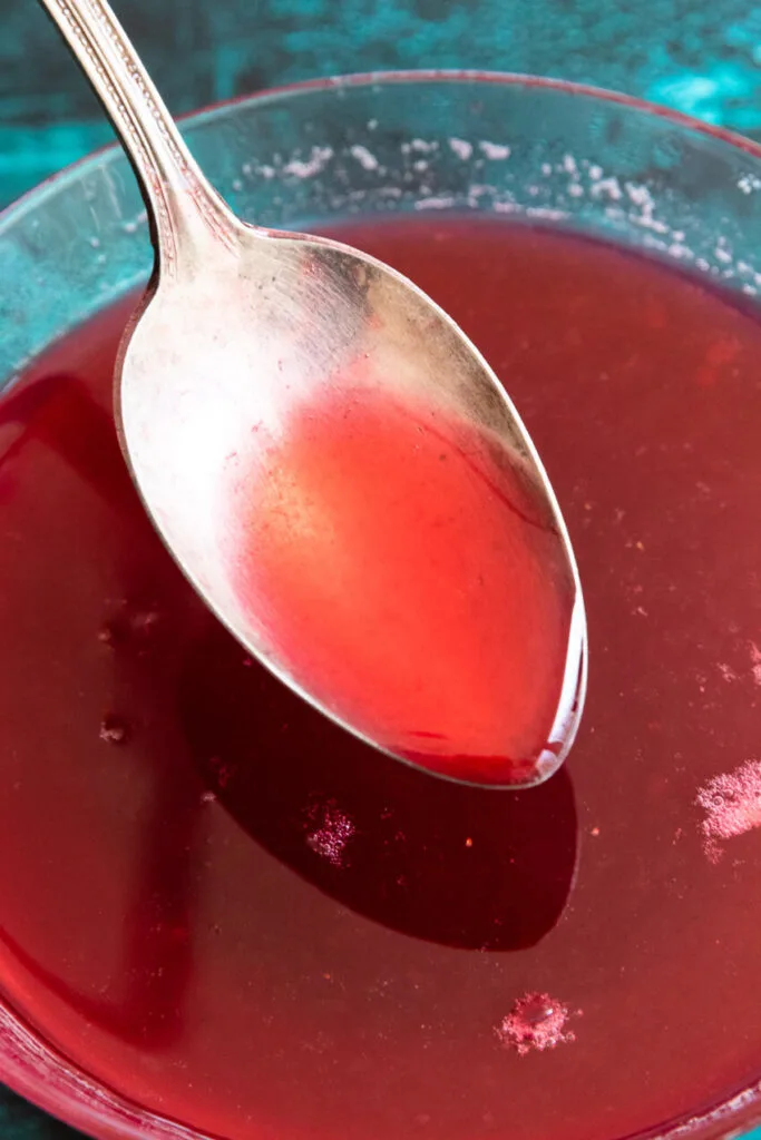 Thickened raspberry simple syrup on a spoon.
