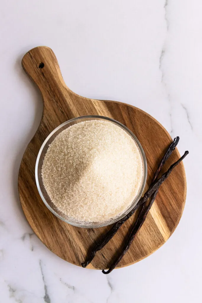 Sugar and vanilla beans on a small cutting board.