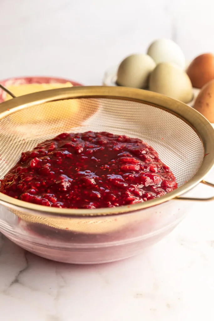 Putting the cooked raspberries through a sieve to remove the seeds.