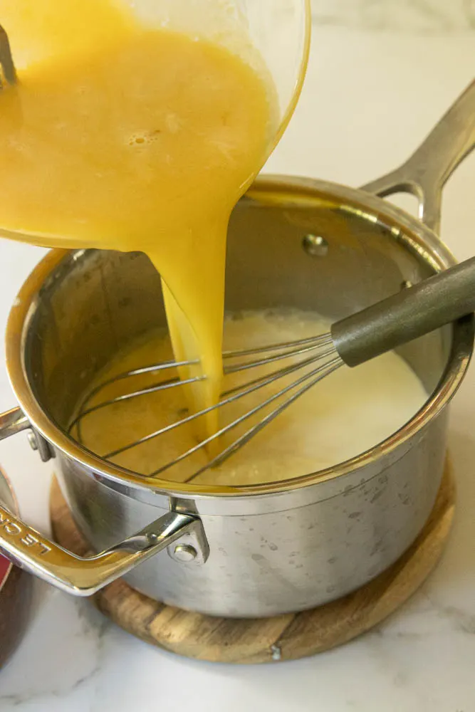 Adding the tempered egg mixture to the pan of warmed milk and cream to finish cooking.